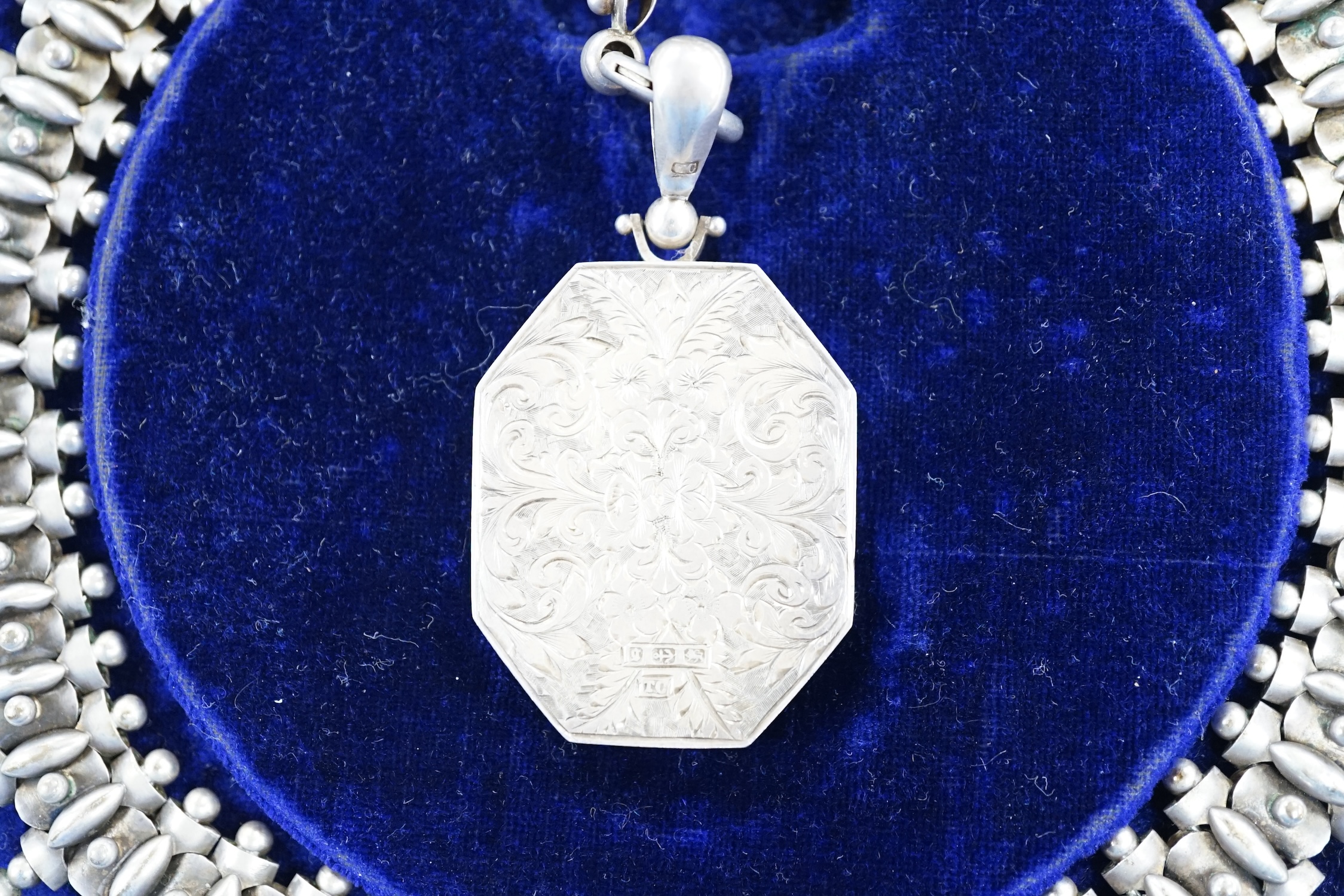 A Victorian silver octagonal locket with engraved aesthetic decoration, Birmingham, 1881, 43mm, on a white metal Etruscan revival chain, 42cm, in fitted case.